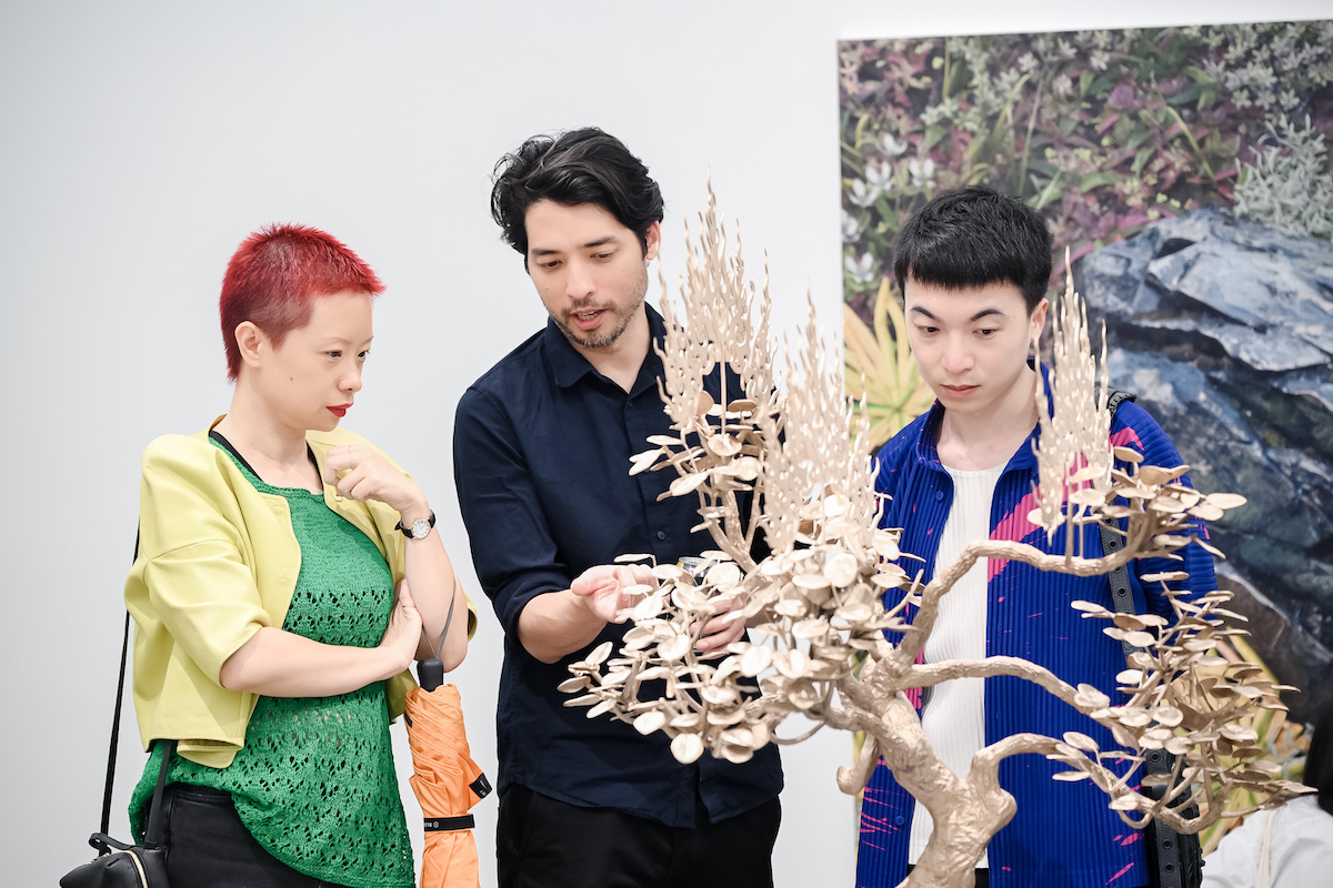 Three Asian people staring at a sculpture resembling a small wooden tree.