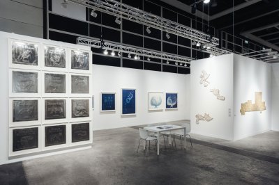 View of an art fair booth showing various artworks made on paper.