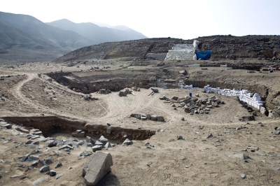 an archaeological site in Caral, Peru, showing rocks, mounds, and some wall fragments