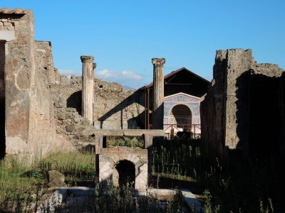 a colorful decorated fountain in Pompeii, surrounded by columns and stone walls