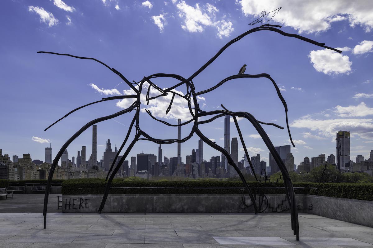 A sculpture of a smiling spider with the New York skyline behind it.