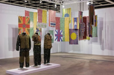 View of an art fair booth showing three mannequins wearing clothes, behind which are various hanging woven flags.