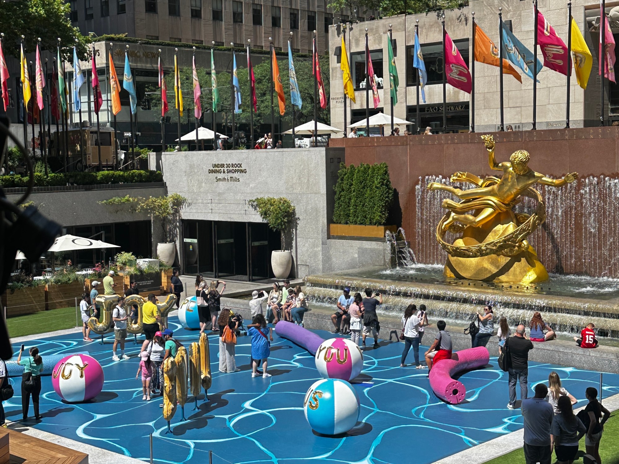 Grownups and children play in Joel Mesler's pool party-themed installation at 30 Rockefeller Park Plaza.