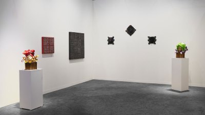 View of an art fair booth showing two sculptures of women's heads on plinths on either side, with wall-hung works in between them.