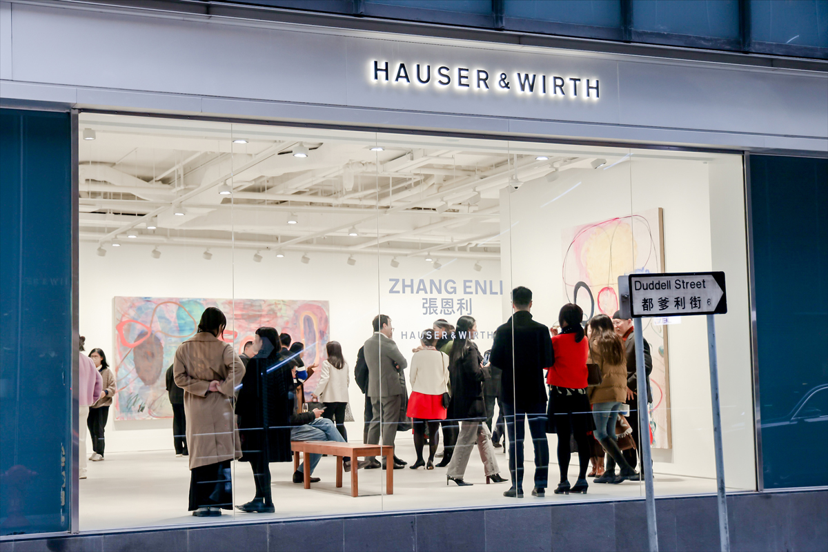 View of people in an art gallery with paintings on the wall. Above reads 'Hauser & Wirth' and a sign for 'Duddell Street' in English and Chinese characters.