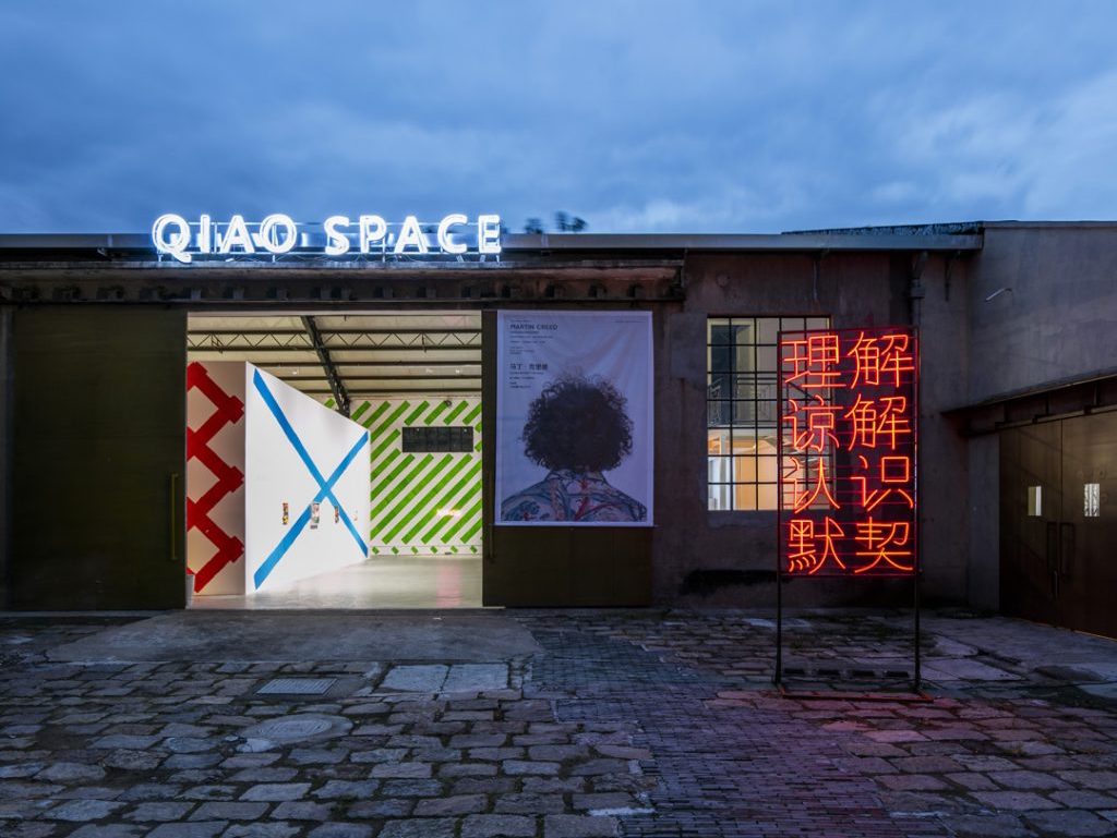 A gallery with the lit-up words 'QIAO SPACE' above its doorway.